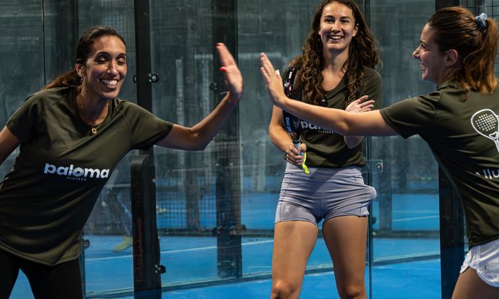 Trois de nos participantes partagent un sourire et un geste de complicité sur le terrain de padel